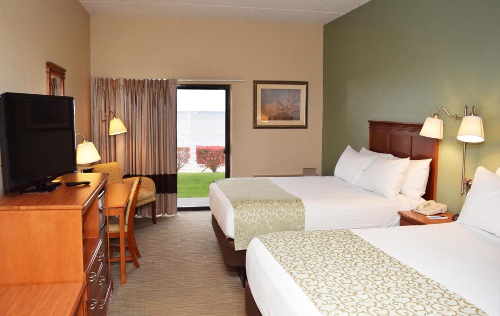 a hotel room with two beds and a flat screen tv at Beachfront Hotel Houghton Lake in Houghton Lake