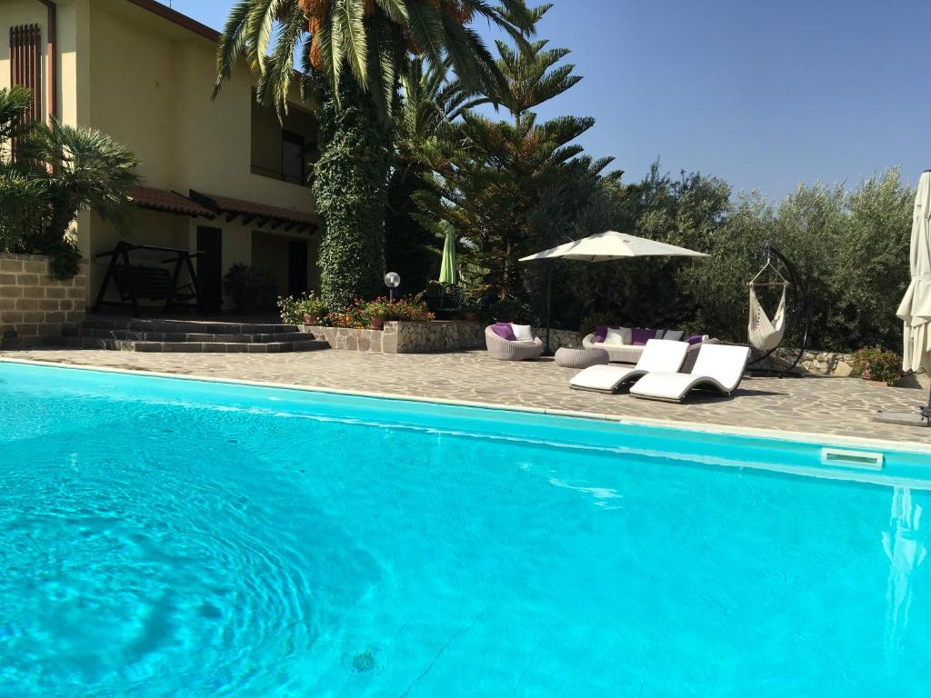 a blue swimming pool with chairs and an umbrella at Poggio Delle Palme in Campobello di Licata