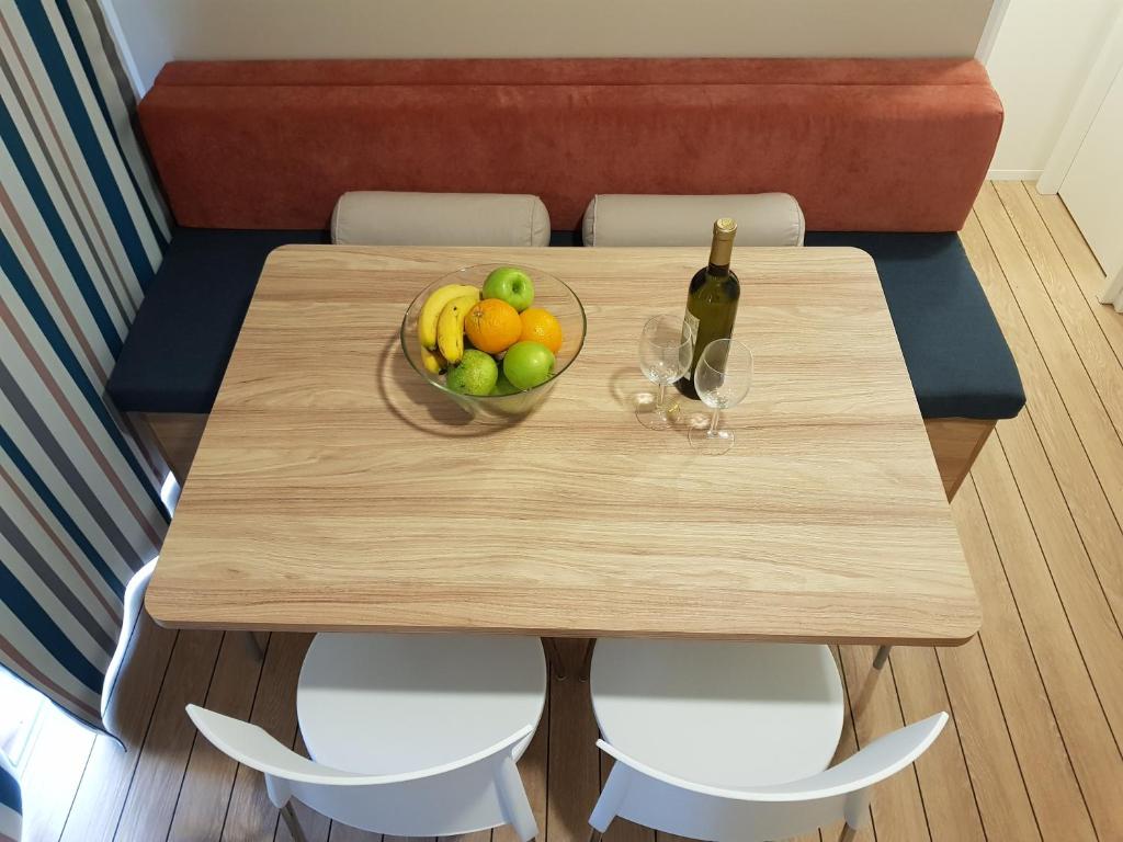 a wooden table with a bowl of fruit and a bottle of wine at Mobile Homes Banko in Bijela Uvala and Zelena laguna in Poreč