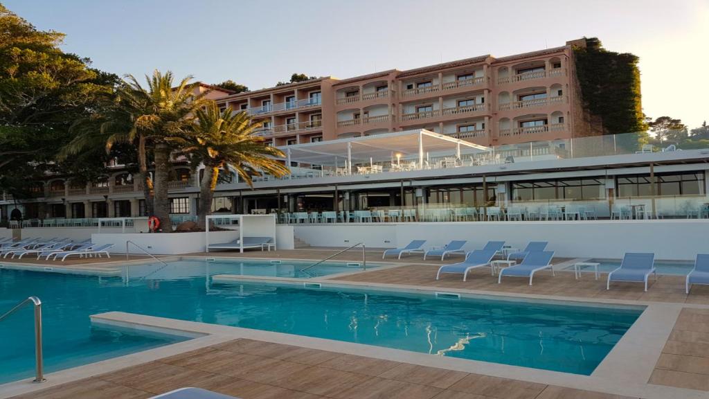 un hotel con piscina con sillas y un edificio en Hotel Na Taconera, en Cala Ratjada