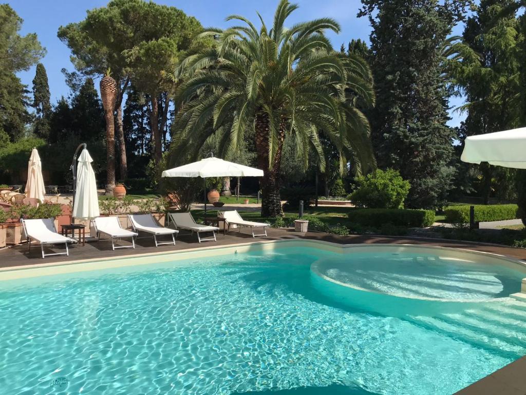 una piscina con sillas, sombrillas y palmeras en Villa Rosella Resort en Roseto degli Abruzzi