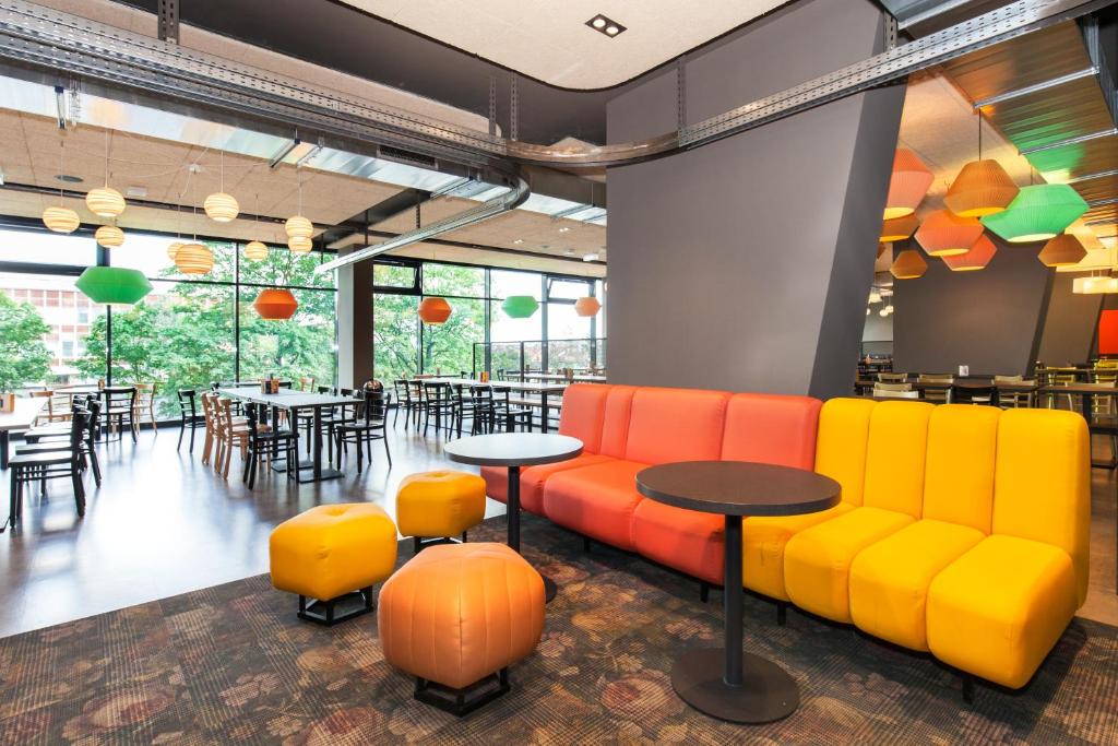 a restaurant with orange and yellow chairs and tables at a&o Prague Rhea in Prague