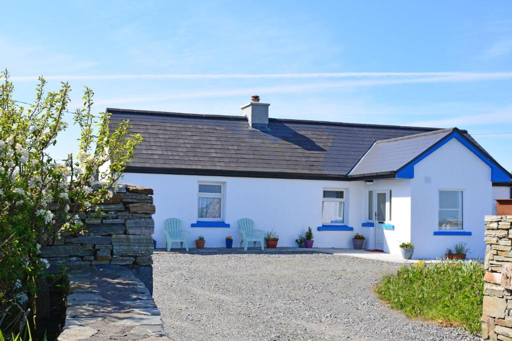 een wit huis met blauwe stoelen ervoor bij Cottage 312 - Ballyconneely in Ballyconneely