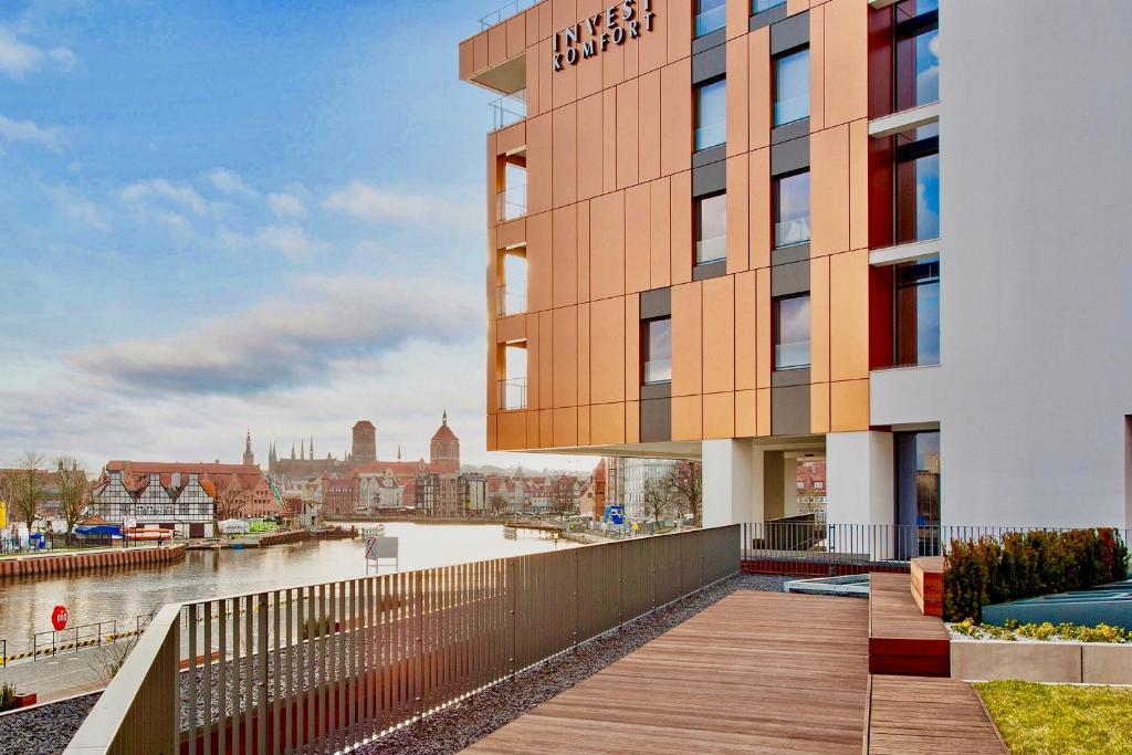 a building with a wooden walkway next to a river at Blue Mandarin Riverside in Gdańsk