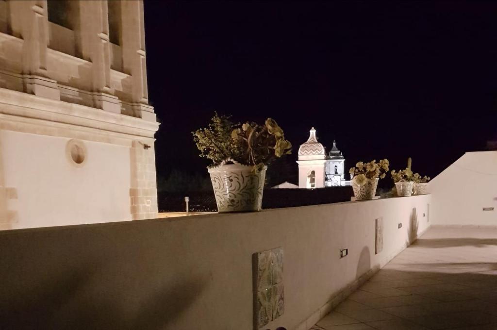 a wall with potted plants and a clock tower at night at B&B Loft Famiglia Arezzo in Ragusa