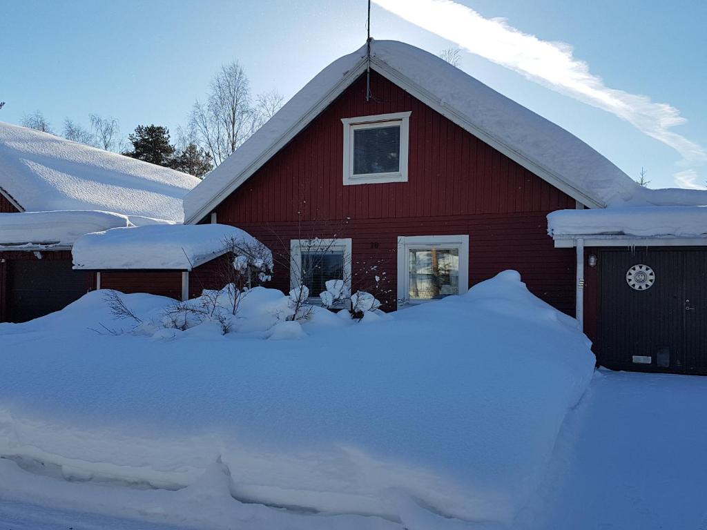een rode schuur bedekt met sneeuw met een berg sneeuw bij Villa Tall in Vidsel