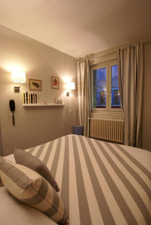 a bedroom with a striped bed with a window at Hotel de la Placette Barcelonnette in Barcelonnette