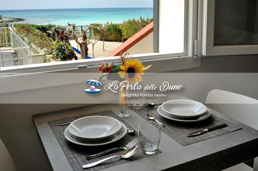 a table with plates and glasses and a window with the ocean at La Perla delle Dune (Sul Mare) in Porto Cesareo