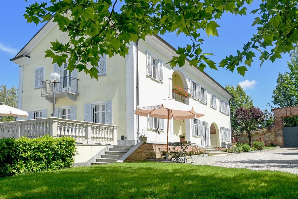 ein großes weißes Haus mit einem Regenschirm im Hof in der Unterkunft Cascina San Bernardo in Magliano Alfieri