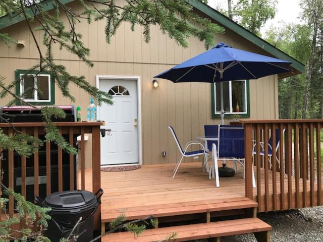 a deck with a blue umbrella and a table and chairs at Peaceful Talkeetna Getaway #1 in Talkeetna