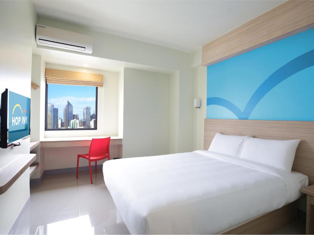 Hop Inn Hotel Alabang Manila في مانيلا: غرفة نوم بسرير ابيض وكرسي احمر