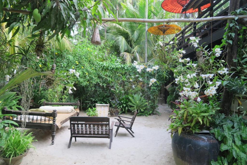 un jardin avec des bancs, des plantes et un parasol dans l'établissement Kipling's Bay Guest house, à Ngapali Beach