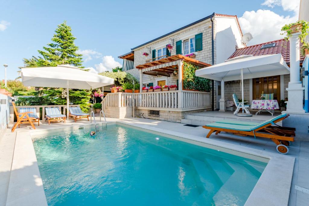 a swimming pool with chairs and umbrellas next to a house at Apartment Villa Camellia - Adults Only in Supetar