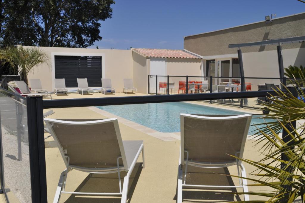a swimming pool with two chairs and a table next to a house at Hotel le Caiman in Pierrelatte