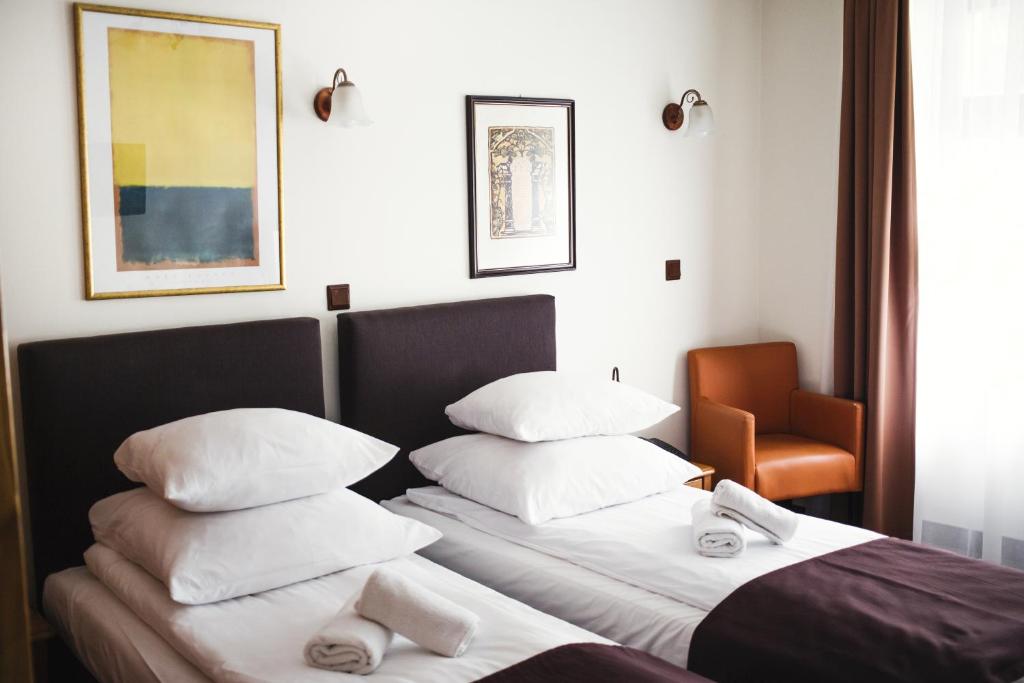 sypialnia z 2 łóżkami z białymi poduszkami i krzesłem w obiekcie Hotel Eden w Krakowie