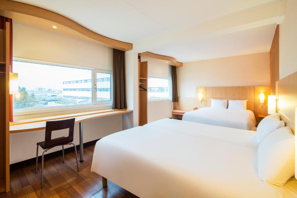 a hotel room with two beds and a desk and a window at Ibis Schiphol Amsterdam Airport in Badhoevedorp