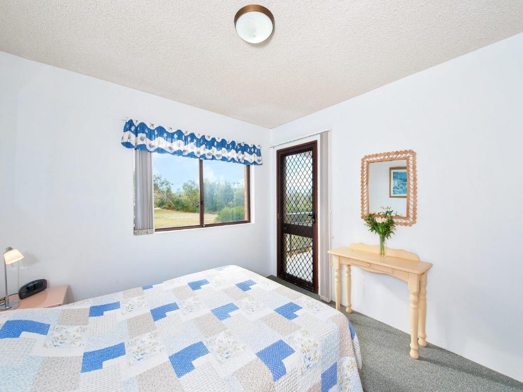 a bedroom with a bed and a table and a window at Foreshore Paradise Nelson Bay in Nelson Bay