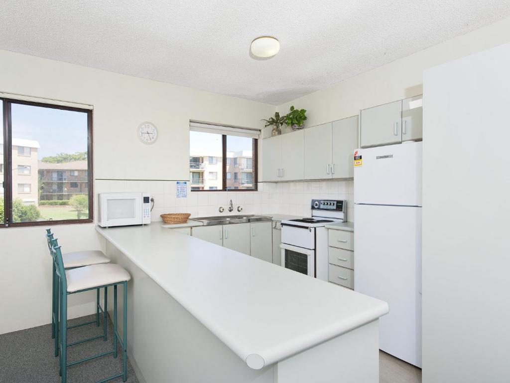 a white kitchen with a counter and a refrigerator at Foreshore Paradise Nelson Bay in Nelson Bay