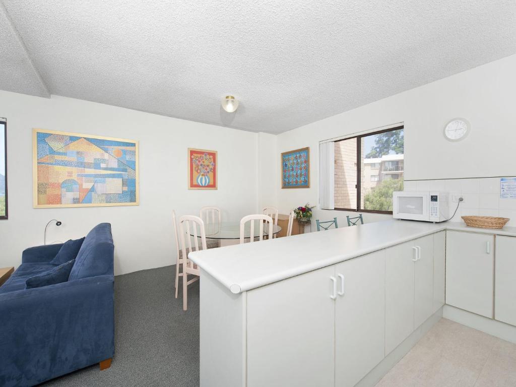 a kitchen and dining room with white cabinets and a blue couch at Foreshore Paradise Nelson Bay in Nelson Bay