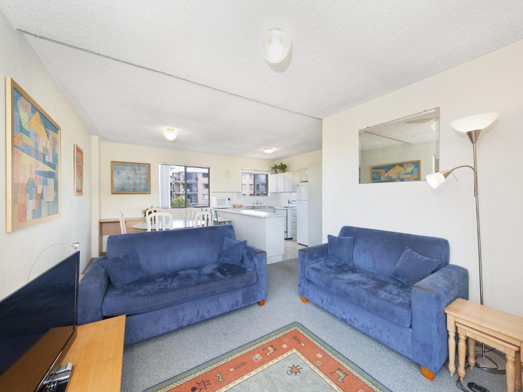 a living room with two blue couches and a kitchen at Foreshore Paradise Nelson Bay in Nelson Bay