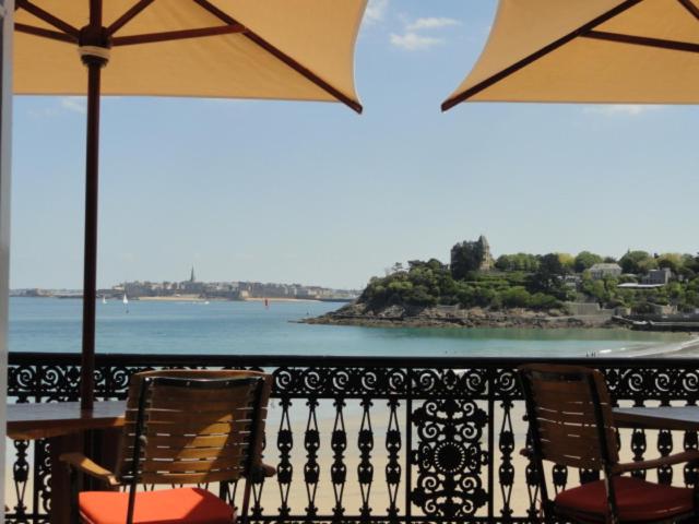 una mesa con 2 sillas y una sombrilla en el balcón en Hotel Villa Reine Hortense, en Dinard