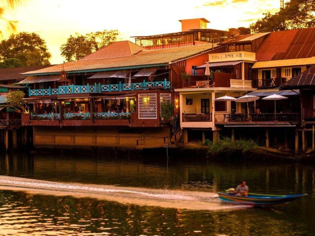 a man in a boat in the water in front of buildings at Tamajun Hotel in Chanthaburi