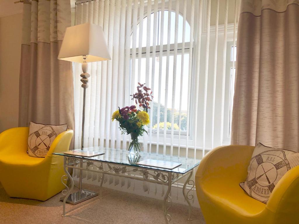 a living room with a glass table and yellow chairs at Arun Sands Rooms in Littlehampton