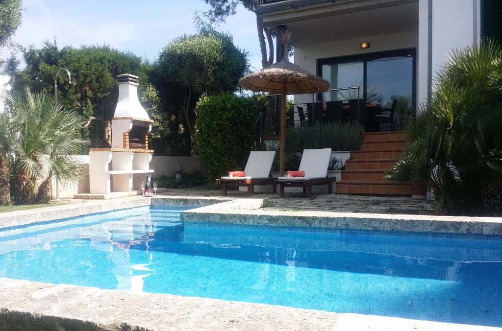 a swimming pool with two chairs and an umbrella next to a house at Villa Pleta in Can Picafort