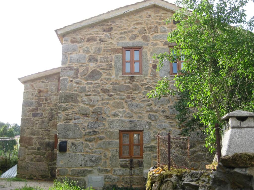 una antigua casa de piedra con ventanas rojas y un árbol en Ares do Montemuro, en Campo Benfeito