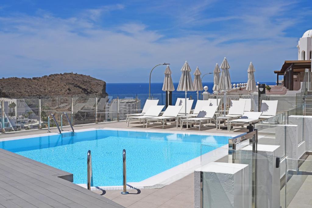 a swimming pool with chairs and umbrellas on a building at Calypso Boutique Apartments in Puerto Rico de Gran Canaria