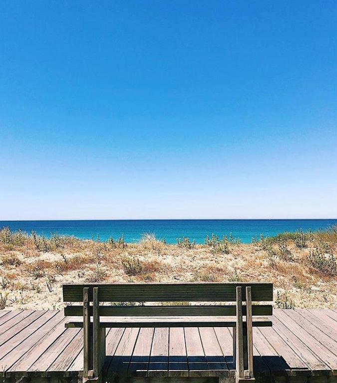 a wooden bench sitting on top of a wooden walkway to the beach at La Toja. Urb. Rueiros. in Isla de la Toja