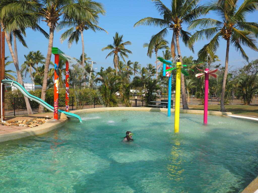 a person in a swimming pool with palm trees at Bowen Holiday Park in Bowen