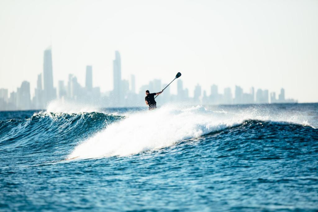 Un hombre montando una ola en una tabla de surf en el océano en Escape to the Coast, en Gold Coast