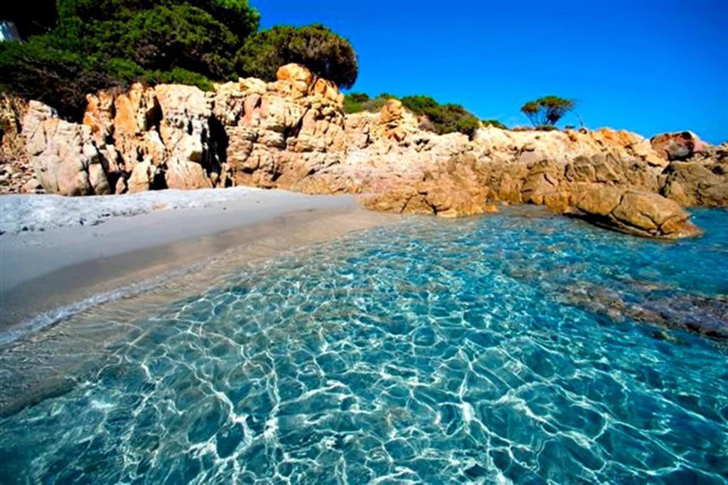 a beach with crystal clear water and a rocky shore at Camping Porto Sosàlinos in Cala Liberotto