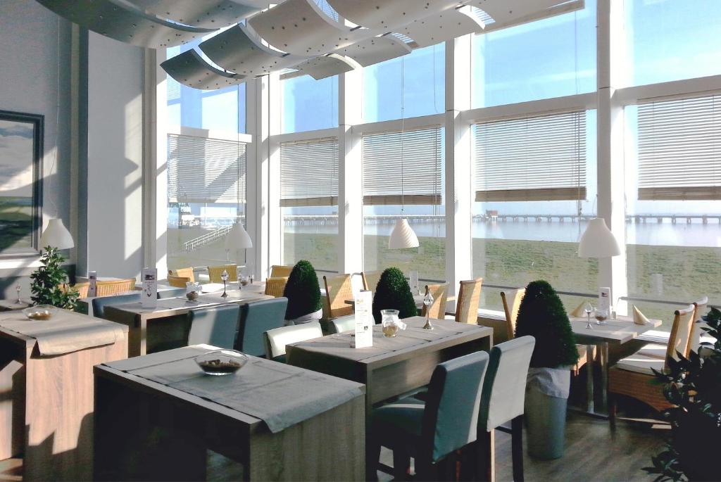 a restaurant with tables and chairs and large windows at Nordseehotel Wilhelmshaven in Wilhelmshaven