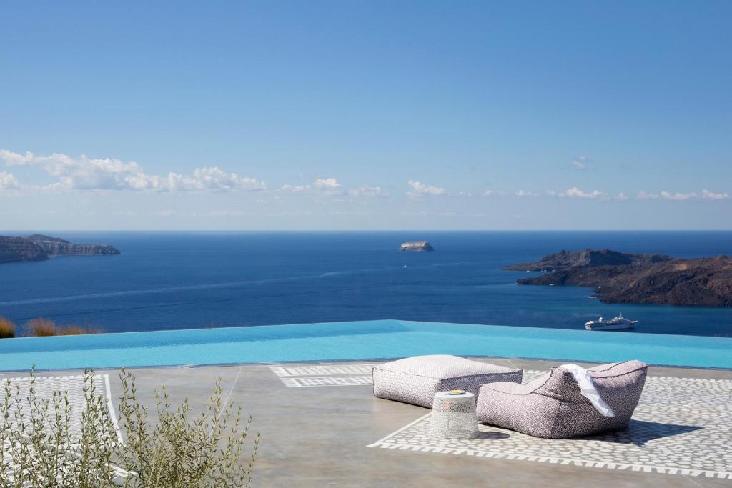 a pool with two chairs and a view of the ocean at Erosantorini Estate in Fira
