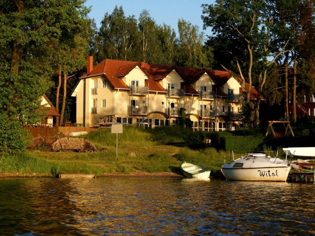 ein großes Haus auf dem Wasser mit einem Boot davor in der Unterkunft Biały Łabędź in Kretowiny
