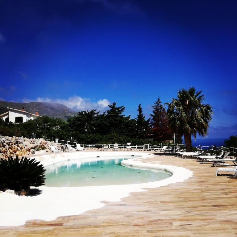 a large swimming pool with chairs and a beach at Baglio Dello Zingaro in Scopello