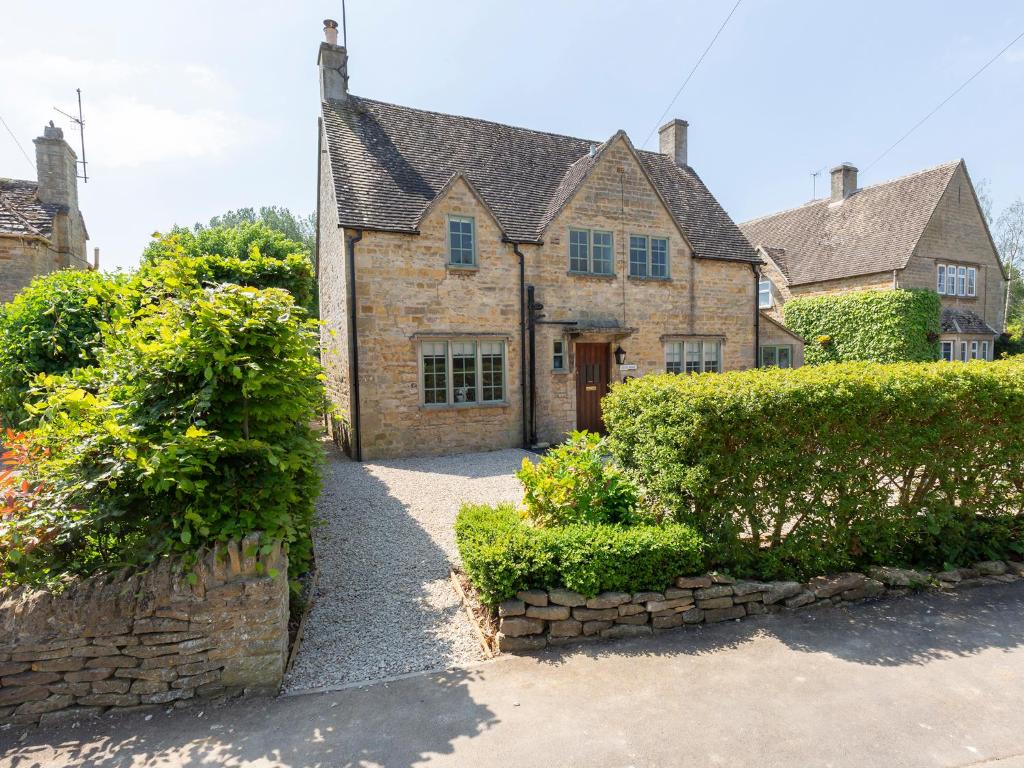 an old stone house with a driveway and bushes at South Winds in Bourton on the Water