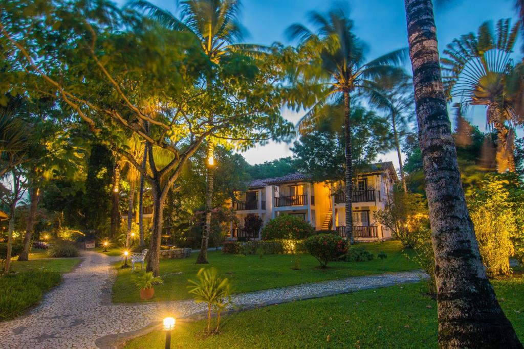 a house in the middle of a yard with palm trees at Manacá Pousada Parque in Arraial d'Ajuda