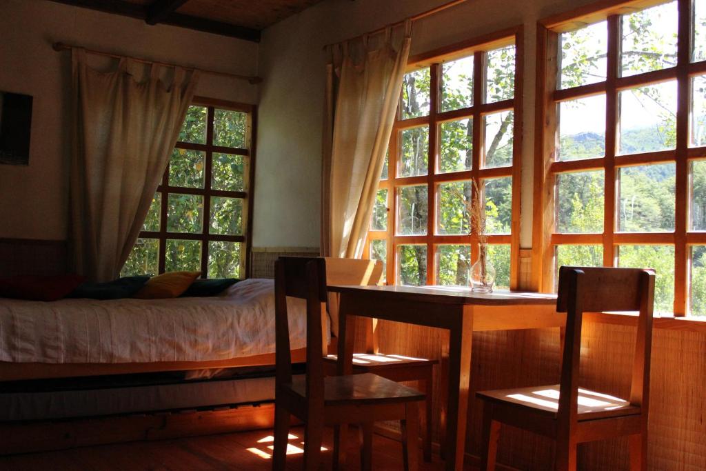 1 dormitorio con cama, mesa y ventanas en Remanso Andino, en Palena