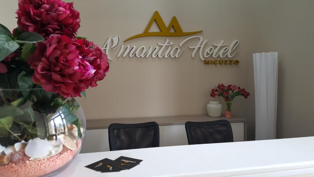 A'MANTIA HOTEL في أمانتيا: إناء من الزهور على طاولة مع علامة فندق aania
