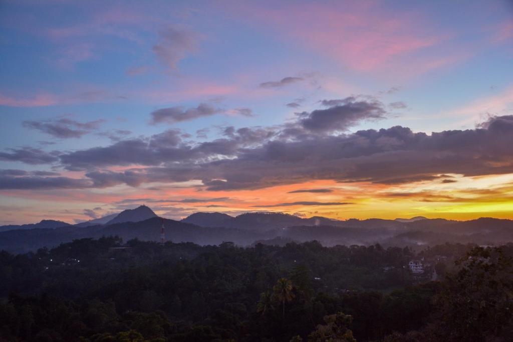 a sunset in the mountains with trees in the foreground at Elegant Hotel in Kandy