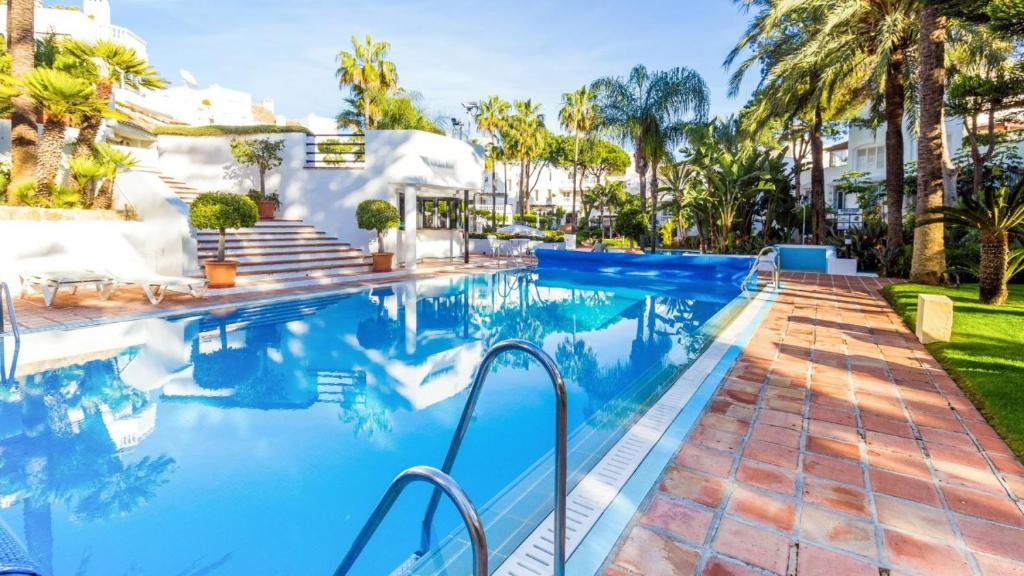 una piscina con agua azul y palmeras en White Pearl Beach - Elviria Playa en Marbella
