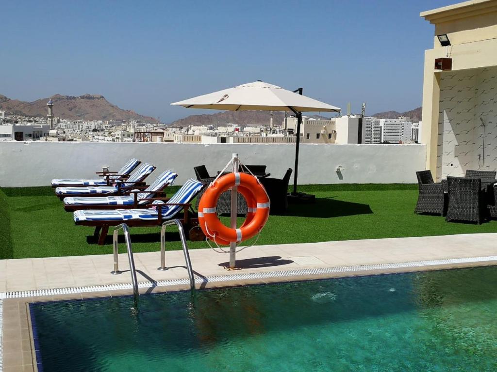 een zwembad met stoelen en een parasol en een oranje vlot bij Golden Tulip Headington in Muscat