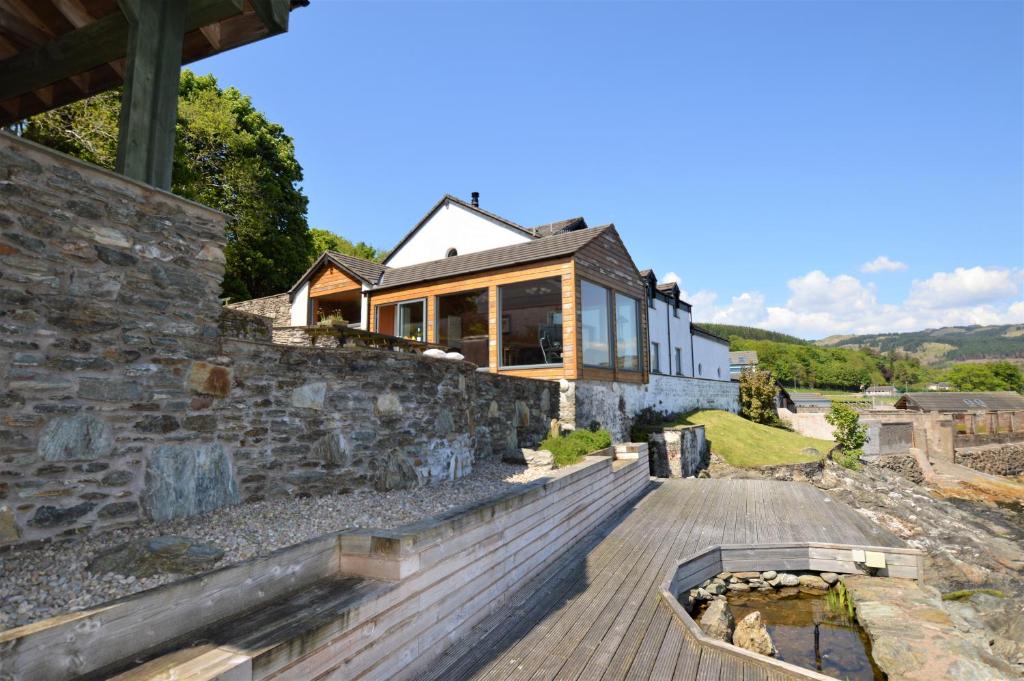 a house with a stone wall and a wooden deck at Taigh na Mara in Kames