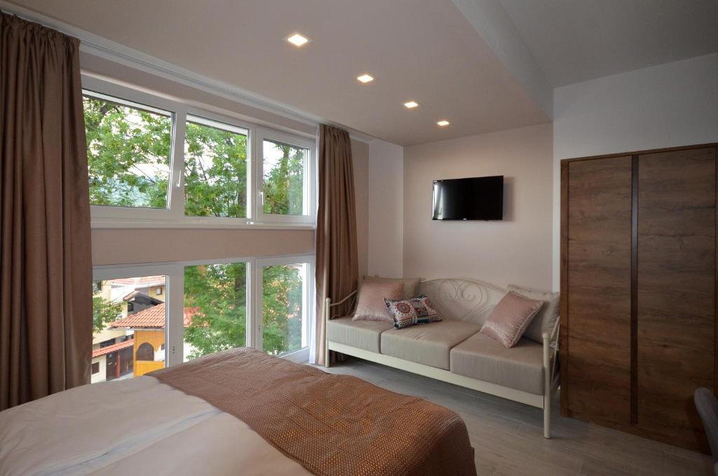 a bedroom with a bed and a couch and windows at Villa Aba apartments in Sarajevo