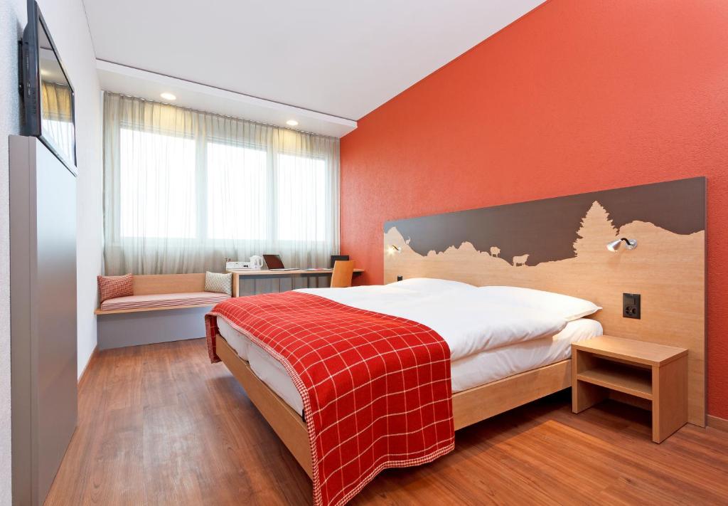 a bedroom with a large bed with an orange wall at SwissEver Zug Swiss Quality Hotel in Zug