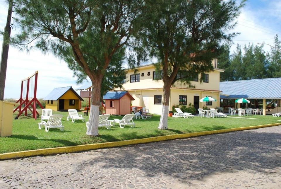 park z białymi krzesłami i drzewami przed budynkiem w obiekcie Residencial Niágara w mieście Arroio do Sal