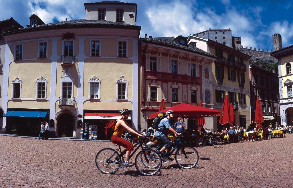 two people riding bikes on a city street at Bellinzona Piazza Collegiata in Bellinzona